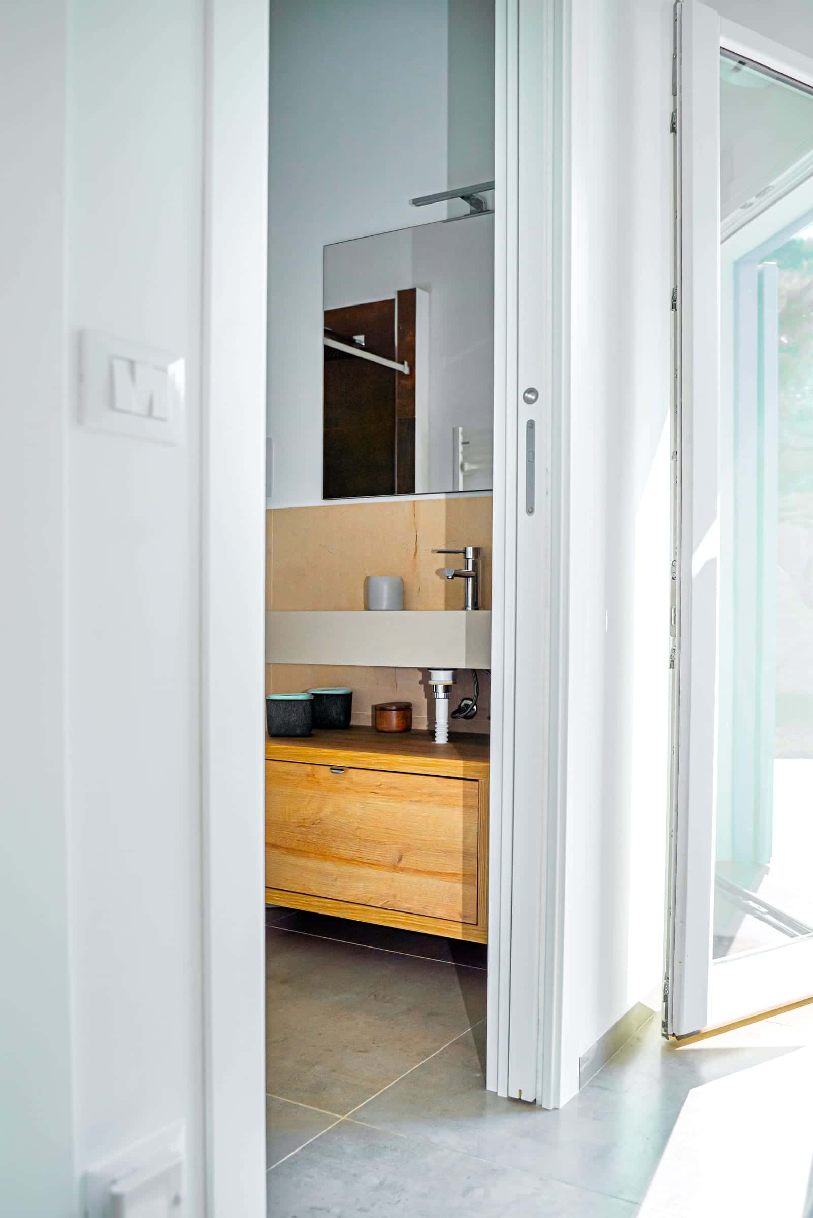 View through a sliding door into a bathroom with a wooden vanity unit and a wall mirror