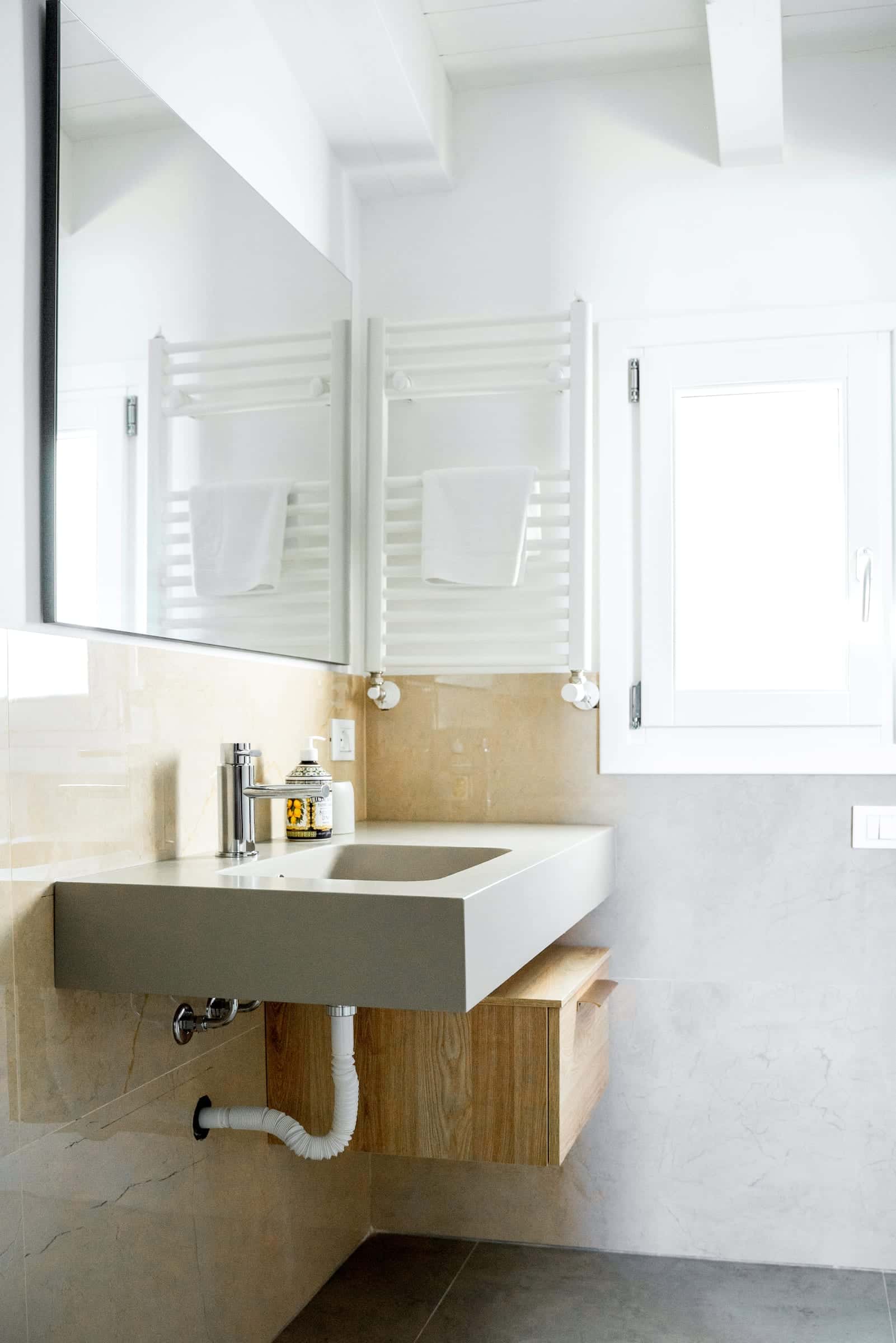 Wall-hung washbasin above a wooden drawer, with a large mirror and a towel radiator beside the window