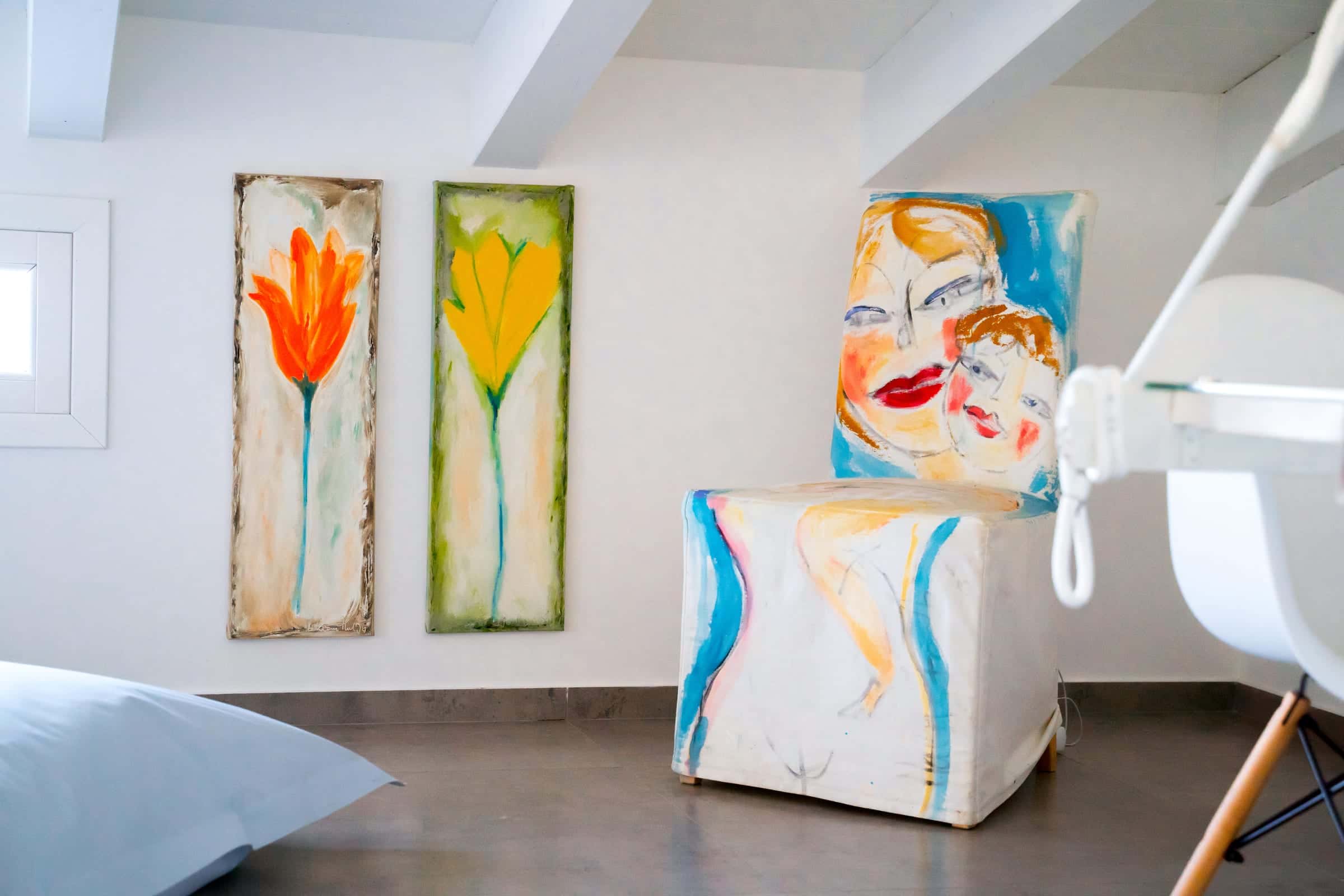 Corner of a bedroom with two flower paintings and a chair with a painted cover