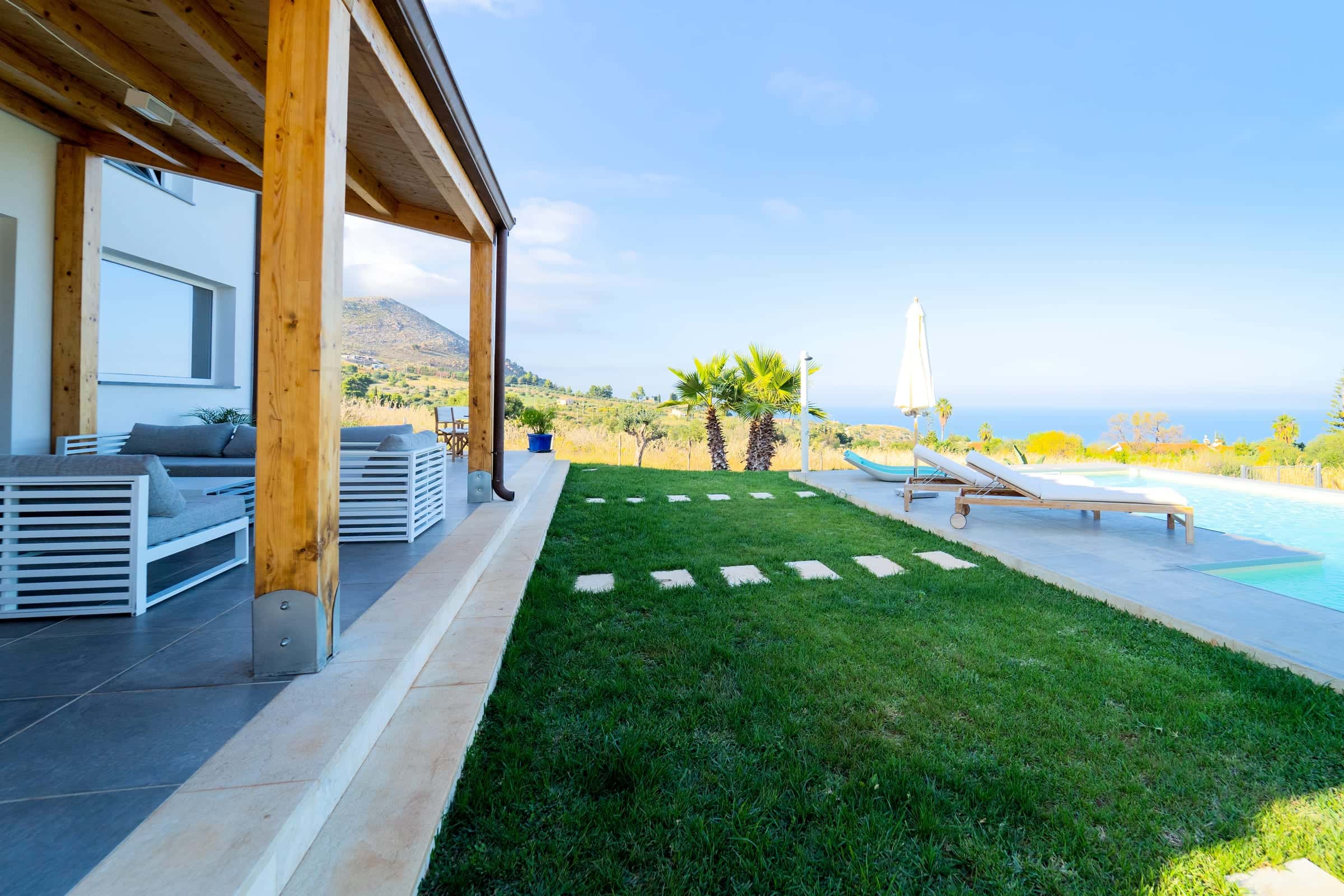 From the covered terrace, stepping stones lead across the lawn to the pool and its sun loungers, with the sea in the distance
