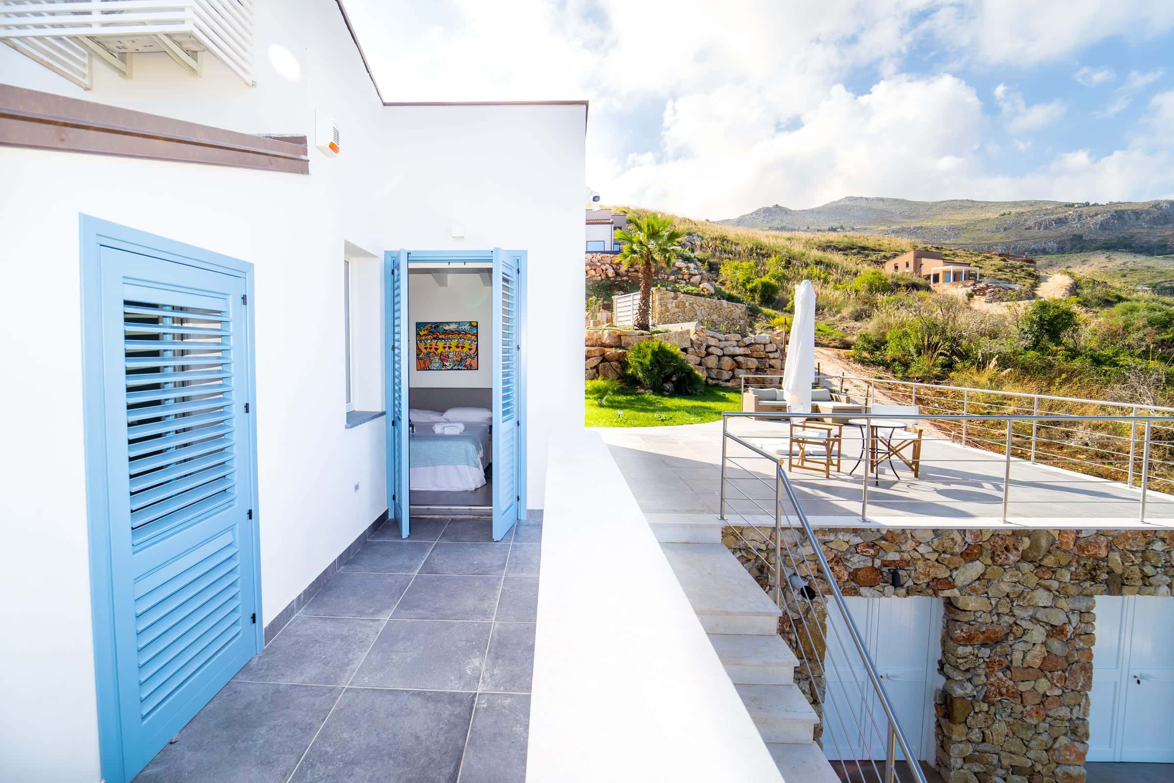 Terrace with blue louvred shutters and an open door into a bedroom; to the right, a second terrace with table and chairs