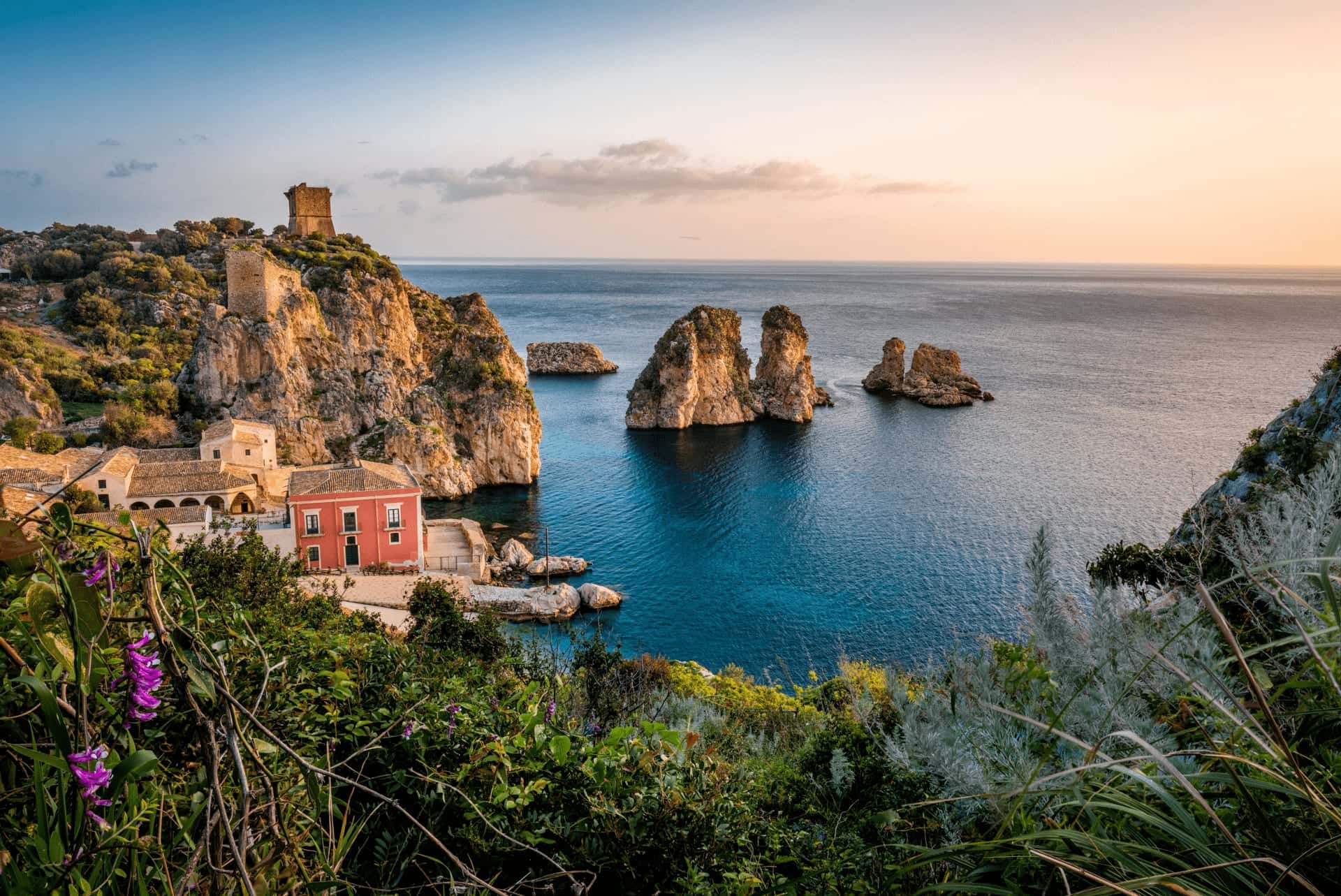 The Tonnara di Scopello and the Faraglioni sea stacks in evening light, with a watchtower on the cliff