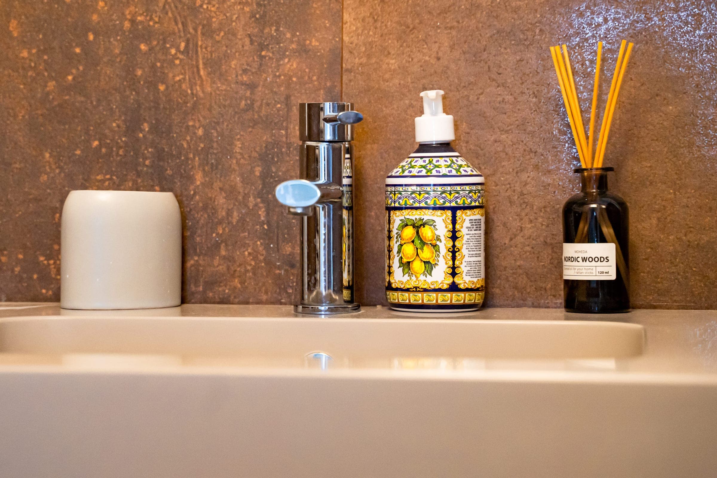 Soap dispenser painted with lemons beside a chrome tap, set against rust-brown tiles