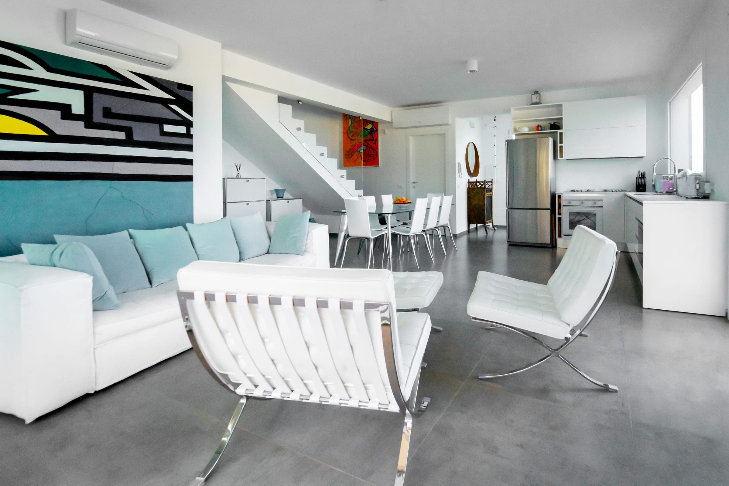 Open-plan living room: a white sofa and armchairs in front, the dining table and kitchen behind