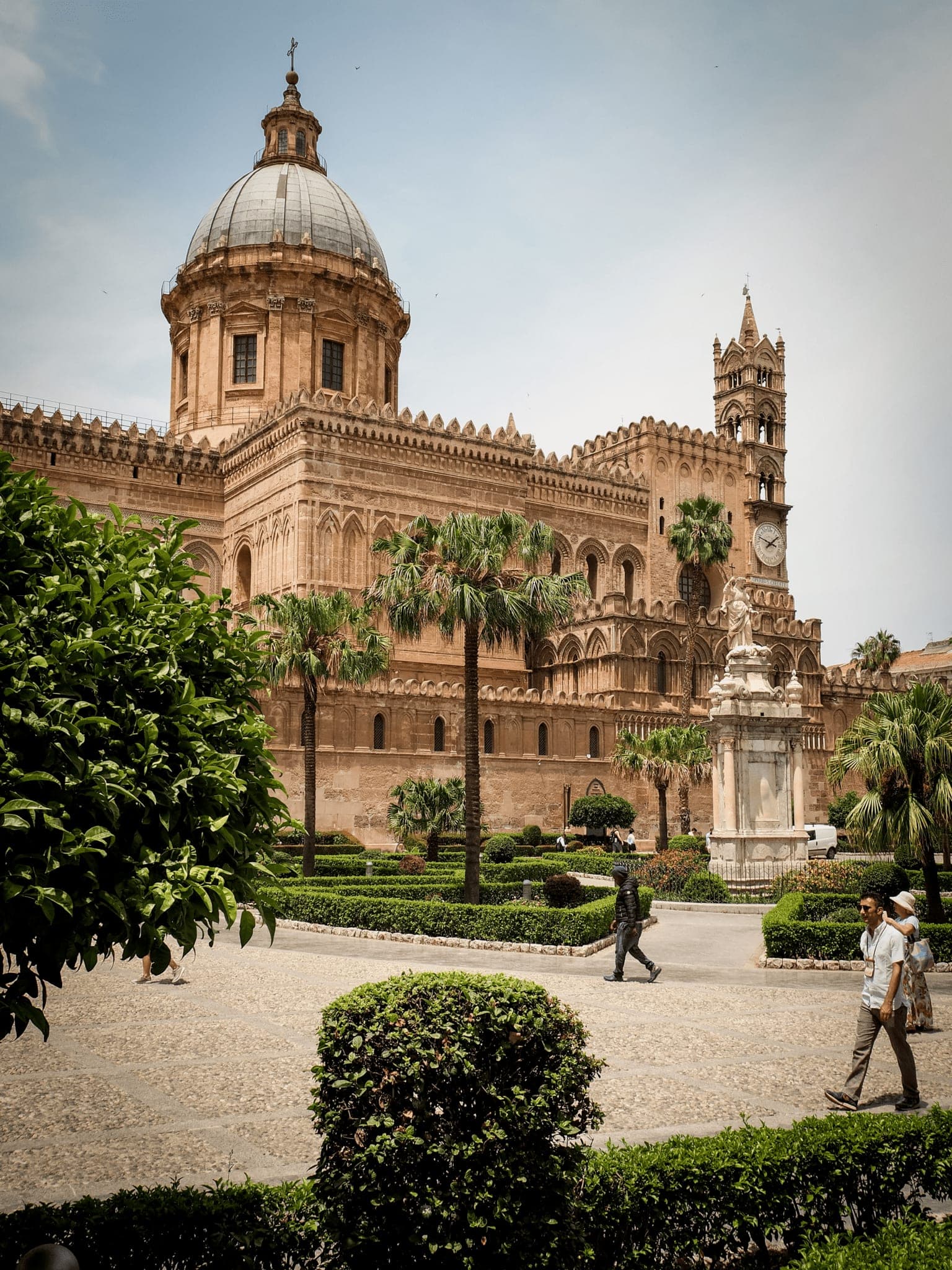 Palermo Cathedral with its dome and clock tower, palm trees and clipped hedges in front